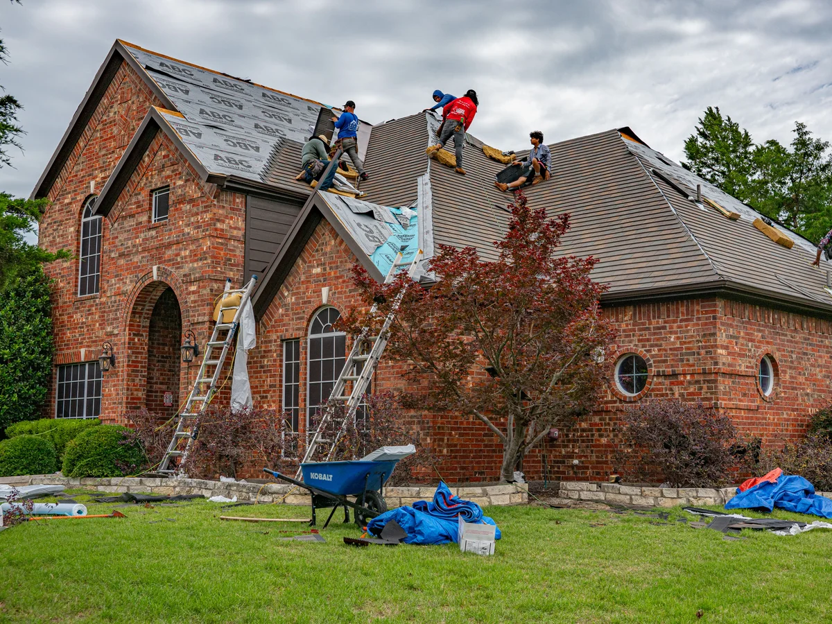 Roofing crew replacing shingles on a brick home's roof